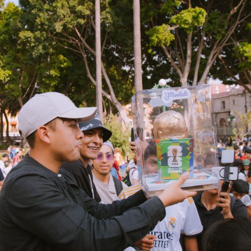 Group of people celebrating with a FIFA World Cup trophy replica in a vibrant outdoor setting.