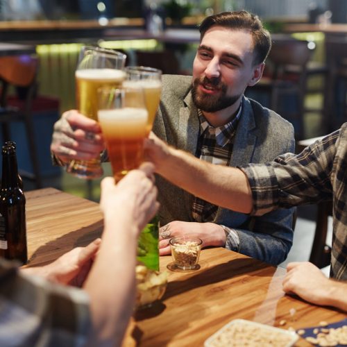 Group of friends toasting with beer glasses while celebrating at a pub.